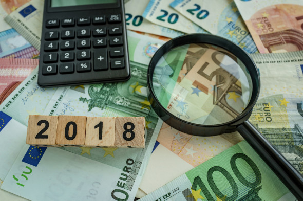financial tax concept as magnifying glass on pile of euro banknotes, calculator and number 2018 on wooden block.